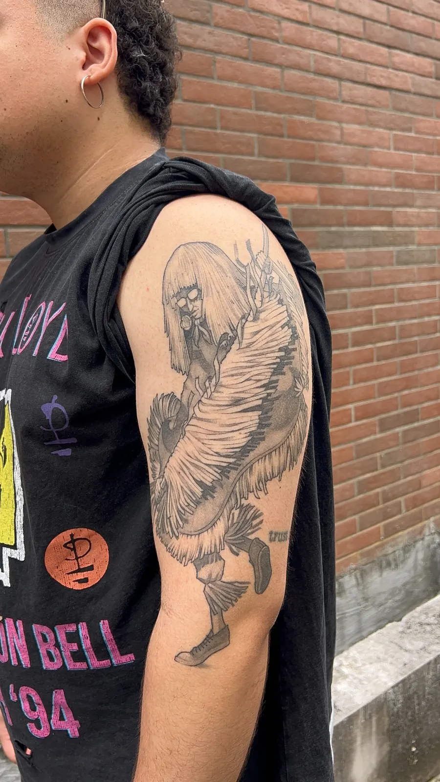 Tatuagem autoral em braço com figura humana e asas